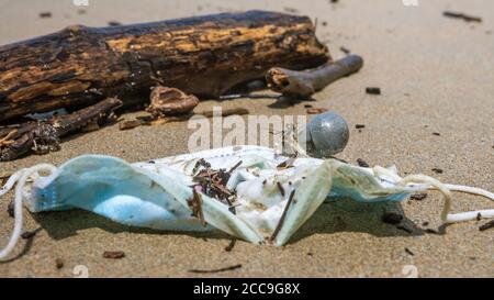 Rifiuti COVID-19. Hermit granchio portare un tubo di plastica vicino a maschere di faccia, mare scartato. Inquinamento ambientale e costiero del coronavirus. Rifiuti in spiaggia Foto Stock