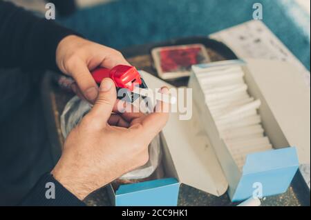 L'uomo fumatore arrotola sigarette di tabacco domestiche usando la macchina rotabile. Primo piano Foto Stock