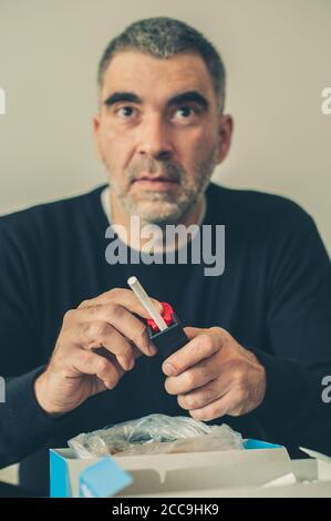 L'uomo fumatore arrotola sigarette di tabacco domestiche usando la macchina rotabile. Primo piano Foto Stock