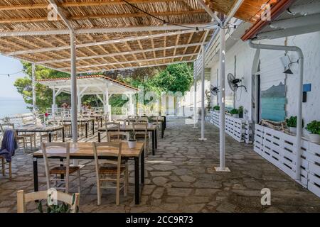CHALKIDIKI, Grecia quasi vuoto sedie taverna e tavoli dopo nuove misure covid-19. Ristorante all'aperto con posti a sedere vicino al mare con alcuni clienti. Foto Stock