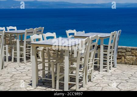 CHALKIDIKI, Grecia taverna vuota sedie e tavoli in legno dopo covid-19 misure. Ristorante con vista mare, area salotto all'aperto senza clienti ad Athytos. Foto Stock