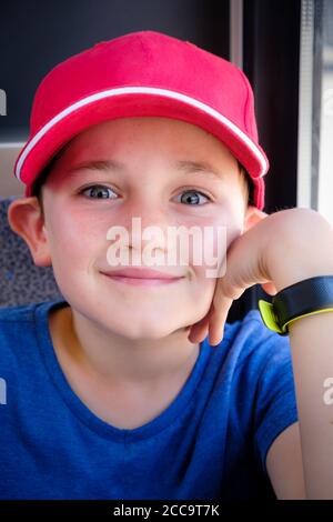 primo piano ritratto di un allegro ragazzo di 9 anni indossando un cappello rosso da baseball che tiene la mano alla sua faccia Foto Stock