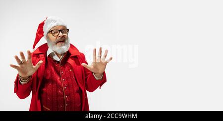 Spaventato, scioccato, palmi aperte. Moderno ed elegante Babbo Natale in abito rosso alla moda isolato su sfondo bianco. Sembra una rockstar. Capodanno e vigilia di Natale, festa, vacanze, moda. Volantino Foto Stock