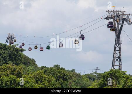 Funivie sull'isola di Sentosa che galleggiano attraverso la lussureggiante vegetazione in fondo. Singapore. Foto Stock