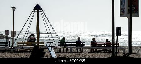 Individui seduti su panchine e divaricarsi dal mare Foto Stock