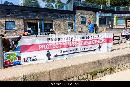 Banner sul lungomare: Si prega di stare a 2 metri di distanza. Lyme Regis, una popolare località balneare sulla Costa Jurassic a Dorset, nel sud-ovest dell'Inghilterra Foto Stock