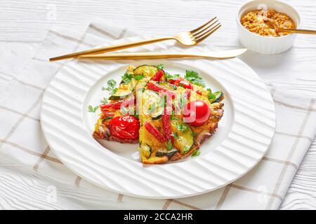 frittata, omelette con zucchine, sottili salsicce affumicate e pomodori ripieni su un piatto bianco su un tavolo di legno con senape sullo sfondo, orizzontale Foto Stock