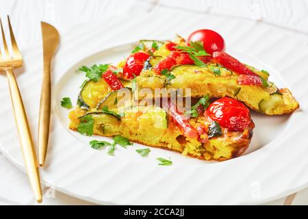 frittata, omelette con zucchine, salsicce affumicate sottili e pomodori ripieni su un piatto bianco su un tavolo di legno, vista orizzontale dall'alto, primo piano Foto Stock