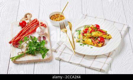 frittata, omelette con zucchine, salsicce affumicate sottili e pomodori ripieni su un piatto bianco su un tavolo di legno, vista orizzontale dall'alto Foto Stock