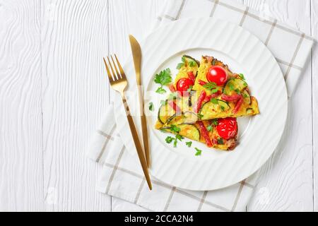 frittata, omelette con zucchine, salsicce affumicate sottili e pomodori ripieni su un piatto bianco su un tavolo di legno, vista orizzontale dall'alto, piatto, libero Foto Stock