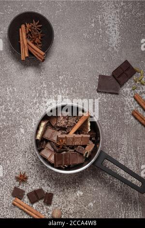 Mucchio di fette di cioccolato scuro e lattiginoso tritato, macinato e trucioli in una pentola con vista dall'alto spezie su sfondo grigio. Foto Stock