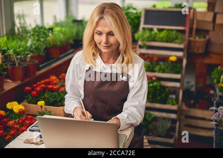 Donna bionda concentrata che lavora in un negozio di fiori Foto Stock