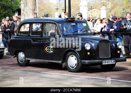 Londra, Regno Unito, 14 aprile 2012: Taxi nero che passa i turisti turistici vicino a Buckingham Palace gate Green Park, che è una destinazione di viaggio popolare Foto Stock