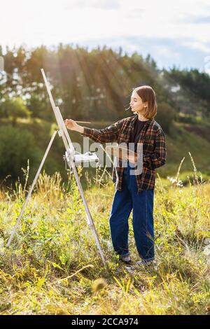 Giovane artista donna dipinge una foto nel parco su una serata estiva di sole Foto Stock