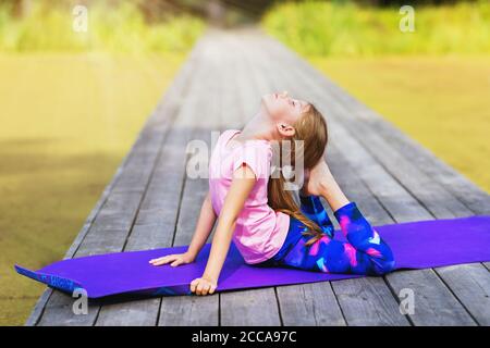 La bambina esegue l'esercitazione ginnastica su un ponte di legno sopra una soleggiata mattina estiva nel parco Foto Stock