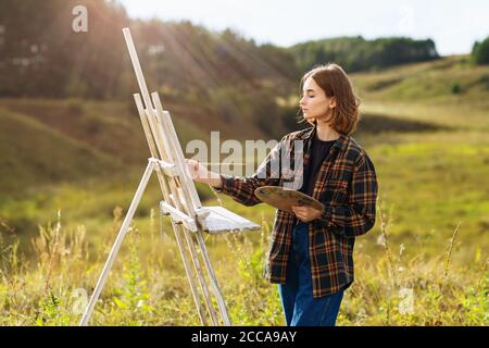 Ragazza artista dipinge una foto all'aperto in un'estate soleggiata sera Foto Stock