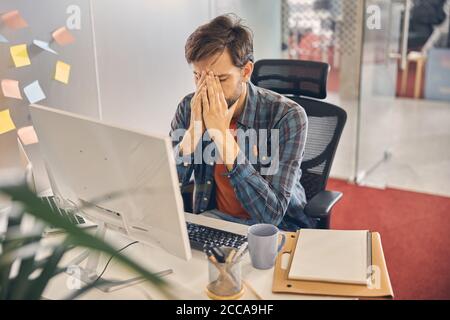 Giovane stanco che lavora in un ufficio moderno Foto Stock