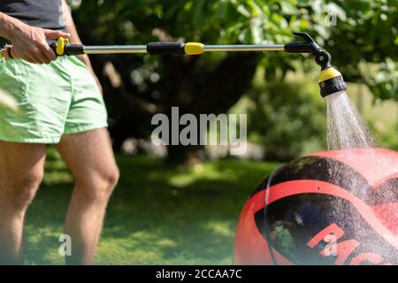 Pulire l'imbarcazione in gomma rossa gonfiata da un giovane uomo. Primo piano su erba verde in giornata di sole. Foto Stock