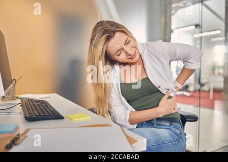 Giovane donna infelice che ha mal di schiena al lavoro Foto Stock