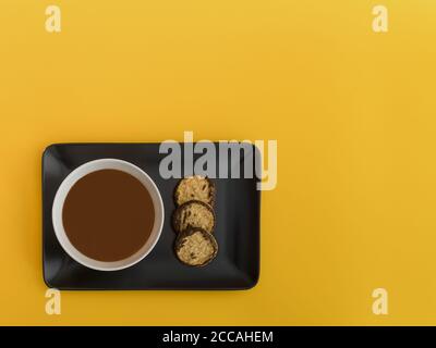 Ciotola di cioccolato su un vassoio nero sfondo giallo. Immagine minimalista dall'alto con spazio disponibile per copiare il testo. Foto Stock