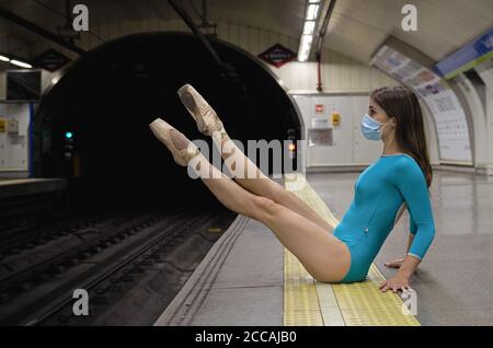 Ballerina femminile indossando abiti blu stretti e facemask danzare su una piattaforma della stazione ferroviaria Foto Stock