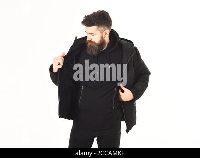 Il ragazzo indossa abiti neri e brutali. Uomo con viso calmo vestendo abiti caldi, isolato su sfondo bianco. Macho con barba e baffi prova su cappotto invernale. Concetto di abbigliamento da uomo. Foto Stock