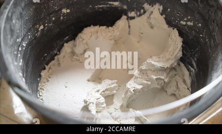 cazzuola con secchio di riempitivo isolato su fondo bianco. Mortaio bianco in un secchio nero. Foto Stock