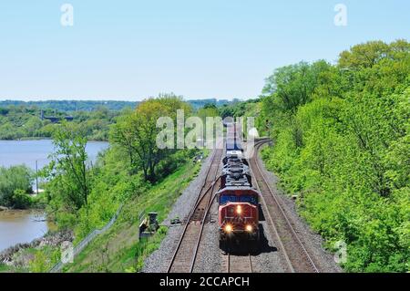 Treno merci CN in arrivo con fari illuminati che trasportano container, autocisterne e cargo che attraversano Hamilton, Ontario, Canada durante il giorno Foto Stock