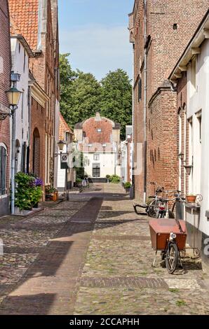 Elburg, Paesi Bassi, 30 luglio 2020: Biciclette, case in mattoni e gesso e pavimentazione in ciottoli in una strada stretta nella vecchia città fortificata Foto Stock