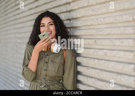 giovane donna mista da corsa con cuffie in abito khaki utilizzando il suo telefono sulla strada Foto Stock