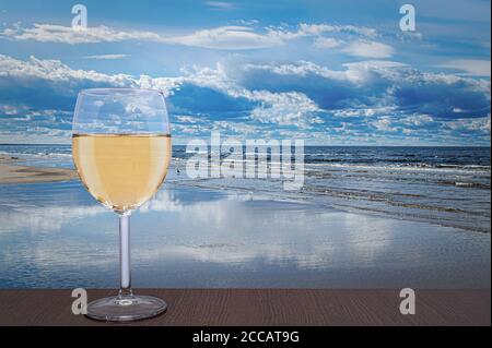 Bicchiere di vino bianco contro il bellissimo paesaggio marino. Mar Baltico durante il giorno di sole con belle nuvole con gabbiani nelle onde a Jurmala, Lettonia Foto Stock