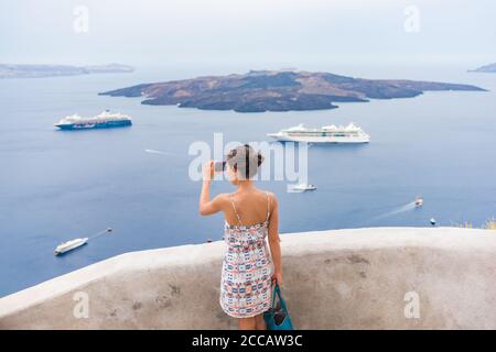 Europa viaggio turista donna scattare foto con il telefono del Mar Mediterraneo a Santorini, Oia, Grecia, con navi da crociera che naviga sullo sfondo dell'oceano Foto Stock