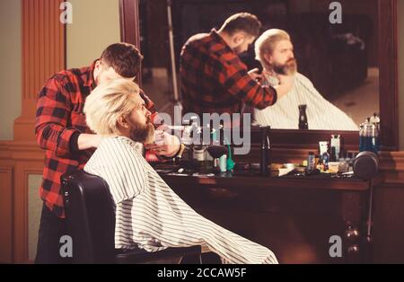 Barber applica olio e cosmetici alla barba del cliente. Foto Stock