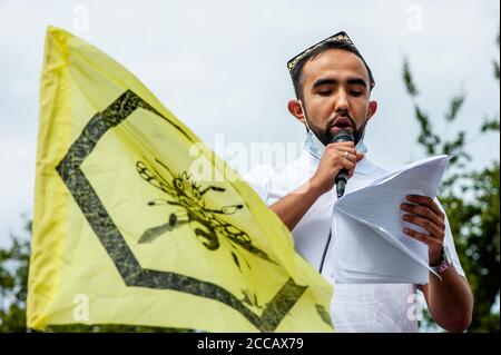 Un uomo Uyghur in piedi accanto a una bandiera XR, facendo un discorso durante la dimostrazione.Extinction Rebellion Fashion Action NL (XRFA) ha collaborato con l'Alleanza organizzativa East-Turkestan per portare l'attenzione pubblica alla discriminazione contro il popolo Uyghur in Cina. I dimostranti hanno iniziato a camminare verso l'ambasciata cinese per una dichiarazione ufficiale, e hanno fatto pressione sul governo olandese e sull'ambasciata cinese affinché agiscano ora e interrompano questa pulizia etnica. Foto Stock