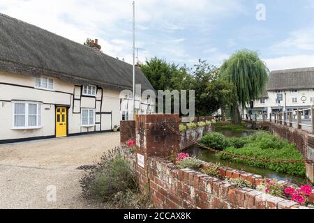 Il fiume Avon attraversa il centro del villaggio di Pewsey, con pittoreschi cottage in legno con tetto di paglia incorniciati a fianco, Wiltshire, Regno Unito Foto Stock