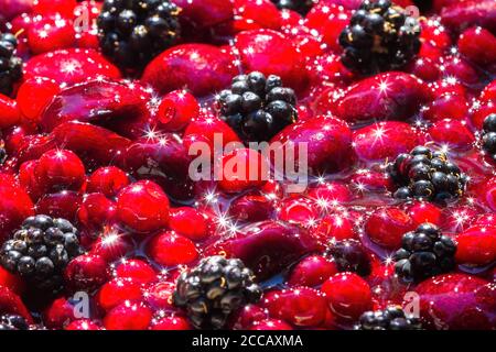 primo piano di una ciotola di bacche miste sotto brillante luce del sole che riflette una bella scintilla sul frutto lucido Foto Stock