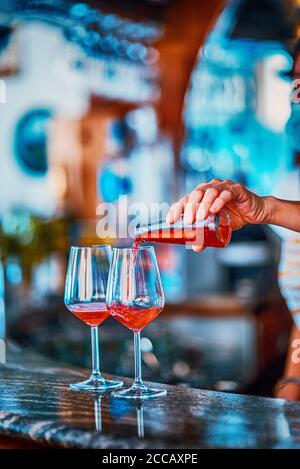 Giovane barista italiano con maschera facciale versando vino bianco in due bicchieri per celebrion Foto Stock