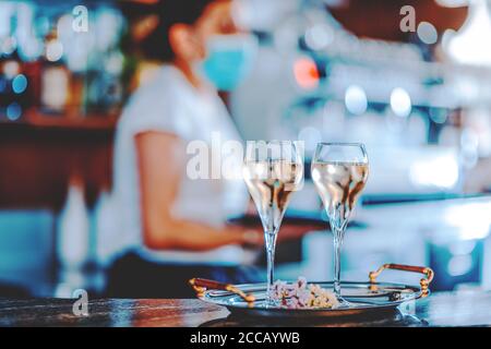 Giovane barista italiano con maschera facciale versando vino bianco in due bicchieri per celebrion Foto Stock