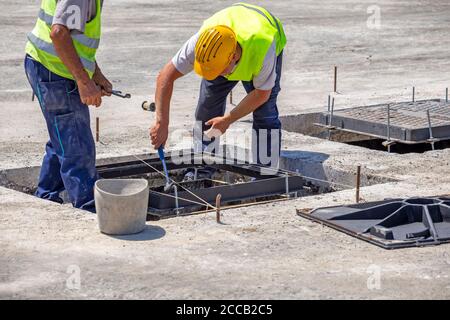 Lavoratori che installano coperture in ferro duttile per proteggere le telecomunicazioni sotterranee Foto Stock