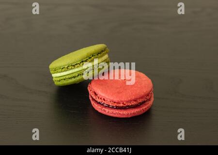 Lamponi dolci e macaroni al pistacchio isolati su sfondo di legno scuro. Pasticceria francese. Piccoli deliziosi dolci francesi. Dessert francese tradizionale Foto Stock