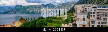 Vista panoramica aerea degli edifici residenziali lungo la costa della Baia di Cattaro e delle montagne sullo sfondo in estate a Dobrota, Montenegro Foto Stock