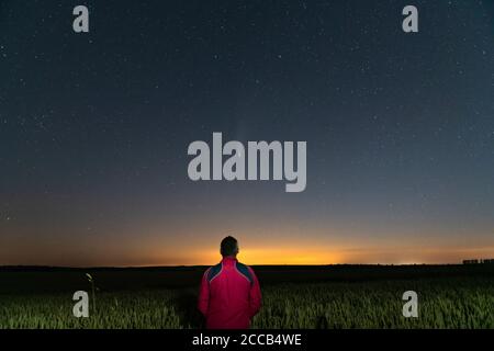 Silhouette di un uomo in piedi di notte in un campo fuori della città. Cielo stellato con cometa Neoswise C/2020 F3 Foto Stock