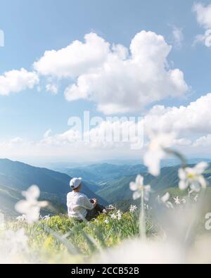 Un turista in abiti bianchi siede in un prato di montagna coperto di fiori di narciso bianchi. Carpazi, Europa. Fotografia di paesaggio Foto Stock