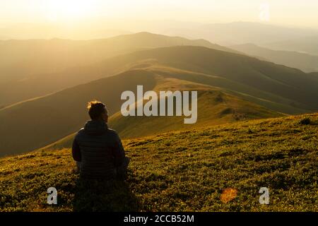 Solo turistico sul bordo della collina di montagna contro lo sfondo di un incredibile paesaggio montano tramonto Foto Stock