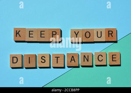 Mantenere la distanza, la frase in caratteri alfabetici in legno 3D isolati su sfondo blu Foto Stock
