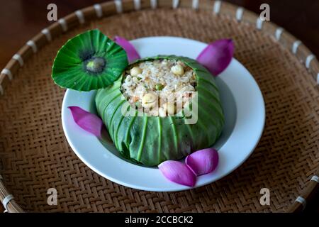 Cibo sano vietnamita per pranzo o cena, riso fritto con verdure, semi di loto, fagioli avvolti in una foglia di loto sullo sfondo del fiore di loto Foto Stock