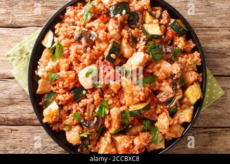 Riso fritto con pollo, zucchine e pomodori ai funghi da vicino in una padella sul tavolo. Vista dall'alto orizzontale Foto Stock