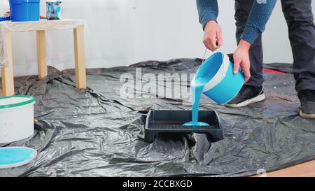 Uomo che versa vernice blu da lattino per la ristrutturazione domestica. Ristrutturazione e costruzione di appartamenti in fase di ristrutturazione e miglioramento. Riparazione e decorazione. Foto Stock
