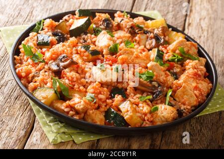 Una pentola di riso con pollo, zucchine e funghi, pomodori, erbe da primo piano in una padella sul tavolo. Orizzontale Foto Stock