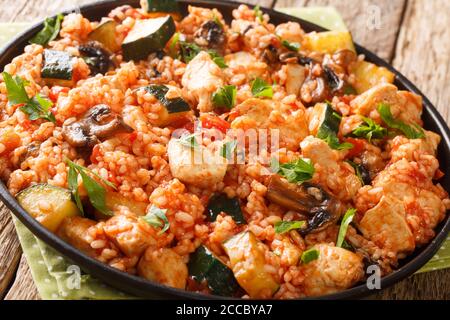 Riso fritto con pollo, zucchine e pomodori funghi primo piano in una padella sul tavolo. Orizzontale Foto Stock